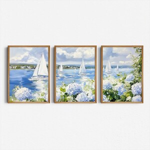 May include: Set of three framed art prints depicting sailboats on a blue sea under a cloudy sky. The artwork features white sailboats, blue water, and blue and white hydrangea flowers in the foreground. The frames are a warm brown color.