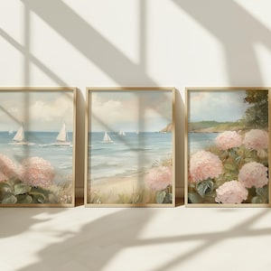May include: Three framed art prints featuring coastal scenes. Each print depicts sailboats on the ocean, a sandy beach, and pink hydrangea flowers. The artwork is in a soft, pastel color palette with a vintage aesthetic.