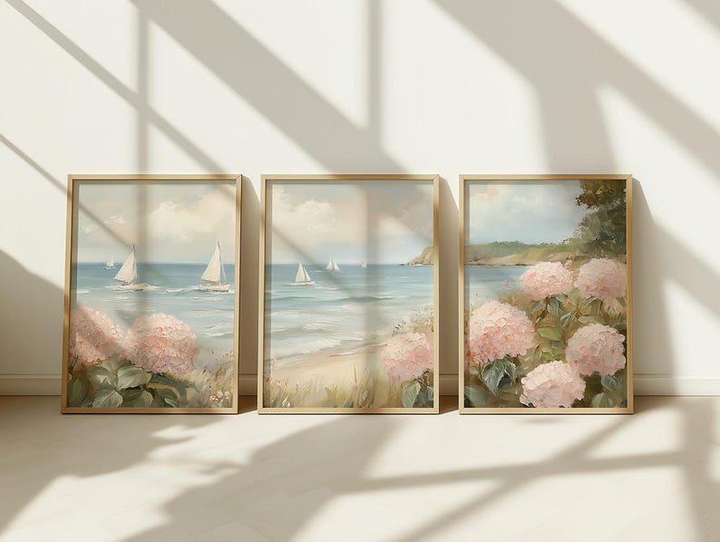 May include: Three framed art prints featuring coastal scenes. Each print depicts sailboats on the ocean, a sandy beach, and pink hydrangea flowers. The artwork is in a soft, pastel color palette with a vintage aesthetic.