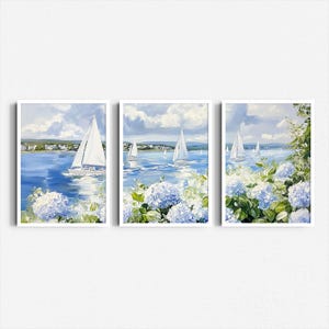 May include: Set of three framed art prints featuring sailboats on a blue sea under a cloudy sky. The artwork includes white sailboats, blue water, and blue and white hydrangea flowers in the foreground. The frames are white.
