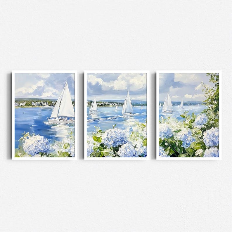 May include: Set of three framed art prints featuring sailboats on a blue sea under a cloudy sky. The artwork includes white sailboats, blue water, and blue and white hydrangea flowers in the foreground. The frames are white.