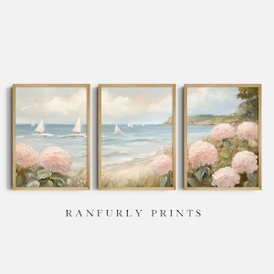 May include: Set of three framed art prints depicting a coastal scene. Each print features sailboats on the ocean, pink hydrangeas, and a sandy beach. The artwork has a soft, pastel color palette and is framed in light wood.