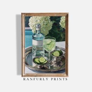 May include: A framed print of a still life featuring a silver tray with a bottle of liquor, a glass of cucumber-infused drink, and a small dish of cucumber slices. The background includes white flowers and a pool. The text "RANFURLY PRINTS" is at the bottom.