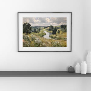 May include: Framed landscape painting depicting a winding river flowing through a valley. The artwork features lush green trees, rolling hills, and a cloudy sky. The painting is in a black frame and is displayed on a white wall.