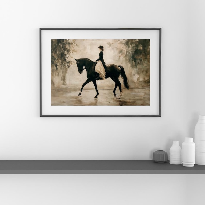 May include: Framed art print of a woman riding a black horse in a classical style. The rider is wearing a dark outfit with a light-colored skirt. The background features a blurred, neutral-toned landscape, creating a sense of depth and movement.