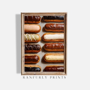 May include: A framed print depicting an assortment of eclairs with diverse toppings, such as chocolate, vanilla, and pistachio. The pastries are arranged in rows on a light grey surface. The print is labelled "RANFURLY PRINTS" at the bottom.