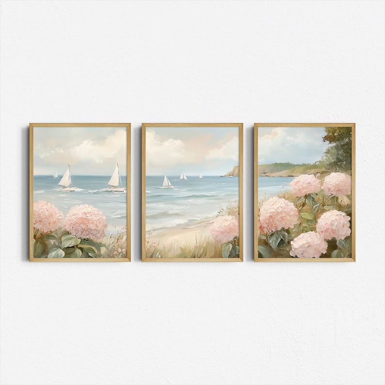 May include: Set of three framed art prints. Each print features a coastal scene with sailboats on the water, a sandy beach, and pink hydrangea flowers. The frames are a light wood color, and the overall style is soft and inviting.