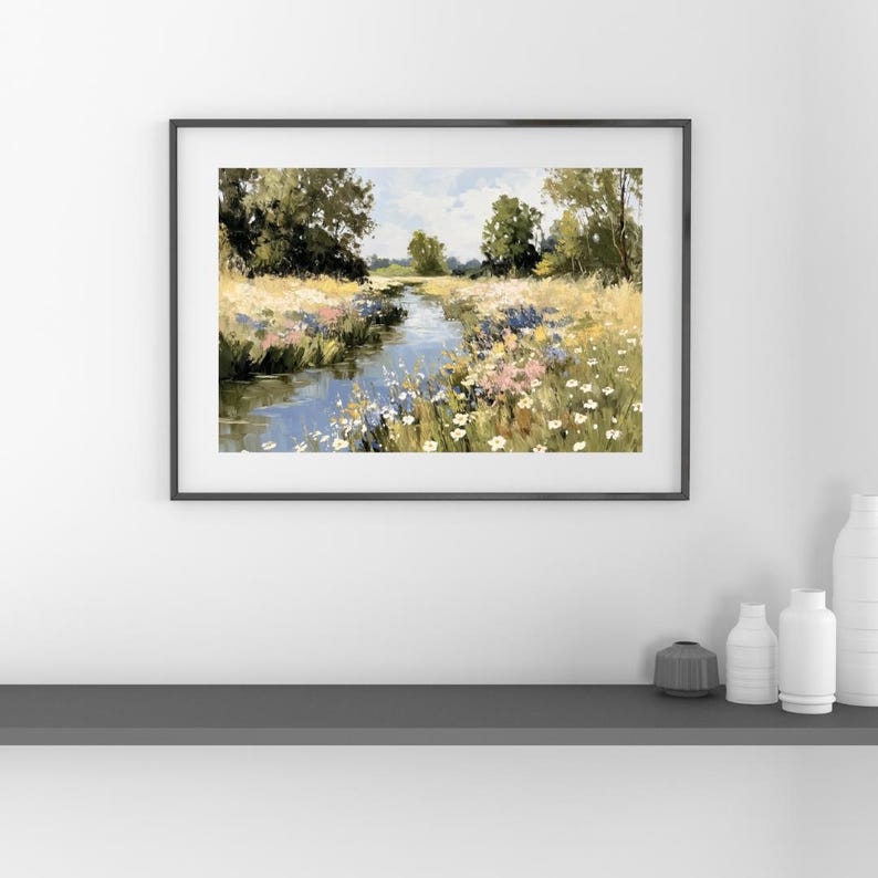 以下が含まれることがあります： 額縁に入った風景画は、野生の花が咲き乱れる野原を縫うように流れる穏やかな川を描いています。 このアートワークは、青、緑、黄、ピンクの色使いで、部分的に曇った空の下、川岸に沿って木々が並んでいます。
