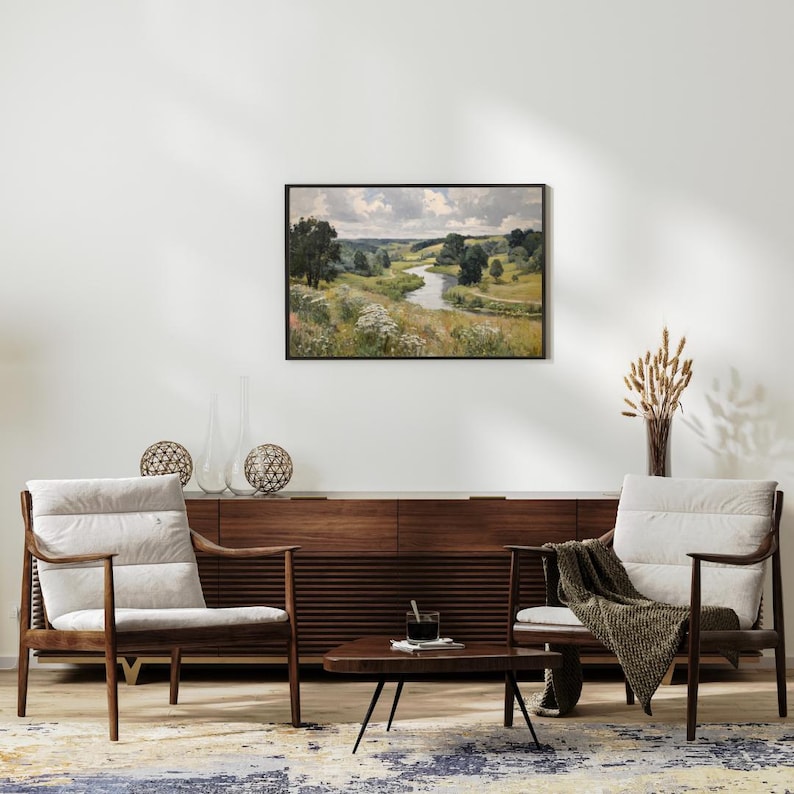 May include: A living room scene featuring two wooden armchairs with cream-colored cushions, a dark wood cabinet, and a small coffee table. A framed landscape painting hangs above the cabinet. Decorative spheres and a vase with dried plants add to the decor.