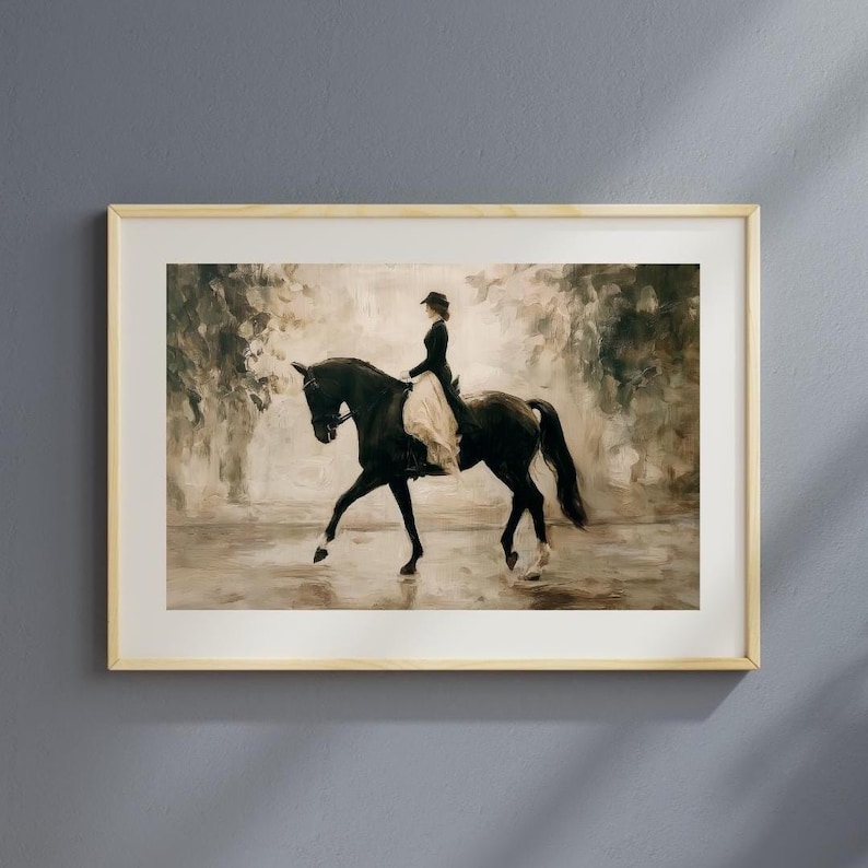 May include: Framed artwork depicting a person riding a black horse in a sepia-toned outdoor scene. The rider is dressed in a dark outfit with a light-colored skirt. The artwork is in a light-colored wooden frame, suitable for home decor.