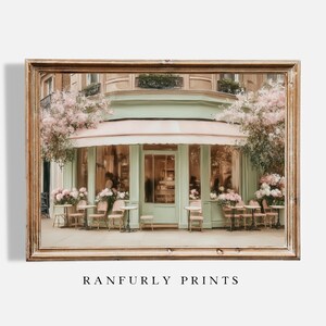 K&ouml;nnte beinhalten: Gerahmter Kunstdruck eines Pariser Caf&eacute;s mit hellgr&uuml;ner Fassade, rosa Markise und Sitzgelegenheiten im Freien. Das Bild zeigt Tische, St&uuml;hle und Blumengestecke. Der Text "RANFURLY PRINTS" befindet sich unten.