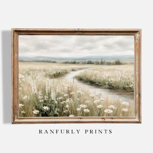 May include: A framed landscape painting depicts a serene field with a winding stream. The artwork features a palette of soft greens, beige, and white, with a cloudy sky. The frame is a light brown color. The text "RANFURLY PRINTS" is at the bottom.