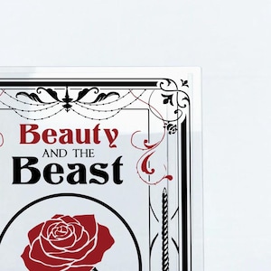 K&ouml;nnte beinhalten: Ein wei&szlig;er Hintergrund mit einem schwarzen und wei&szlig;en Rahmen mit einer roten Rose und dem Text "Beauty and the Beast" in Schwarz und Rot.