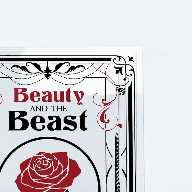 K&ouml;nnte beinhalten: Ein wei&szlig;er Hintergrund mit einem schwarzen und wei&szlig;en Rahmen mit einer roten Rose und dem Text "Beauty and the Beast" in Schwarz und Rot.