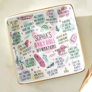 Könnte beinhalten: Ein quadratisches Keramiktablett mit goldenem Rand, das den Text "Sophia's Daily Bible Affirmations" trägt. Das Tablett ist mit pastellfarbenen Formen, Kreuzen und Bibelversen verziert. Das Gesamtthema ist religiös und inspirierend.