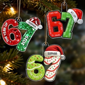 May include: Christmas ornaments shaped like the numbers 6 and 7, with the year 2025. Some ornaments have a Santa hat and the name "Sophia" or "William". The ornaments are red, green, and white, with text like "The Year Of".