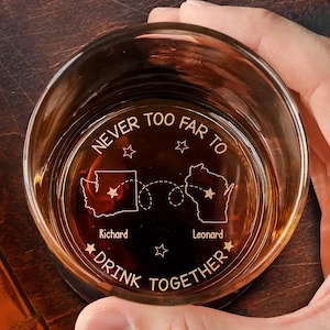May include: A clear glass with a brown liquid inside. The glass has an engraved design with the text "Never too far to drink together" and two star-shaped outlines of the states of Washington and Wisconsin. The text "Richard" and "Leonard" are engraved below the states.