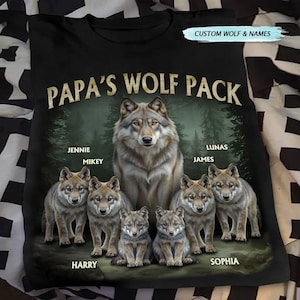 May include: Black t-shirt featuring a wolf pack design. The shirt displays the text "PAPA'S WOLF PACK" in gold lettering, with a large wolf and six smaller wolves. The names "JENNIE", "MIKEY", "LUNAS", "JAMES", "HARRY", and "SOPHIA" are also visible.