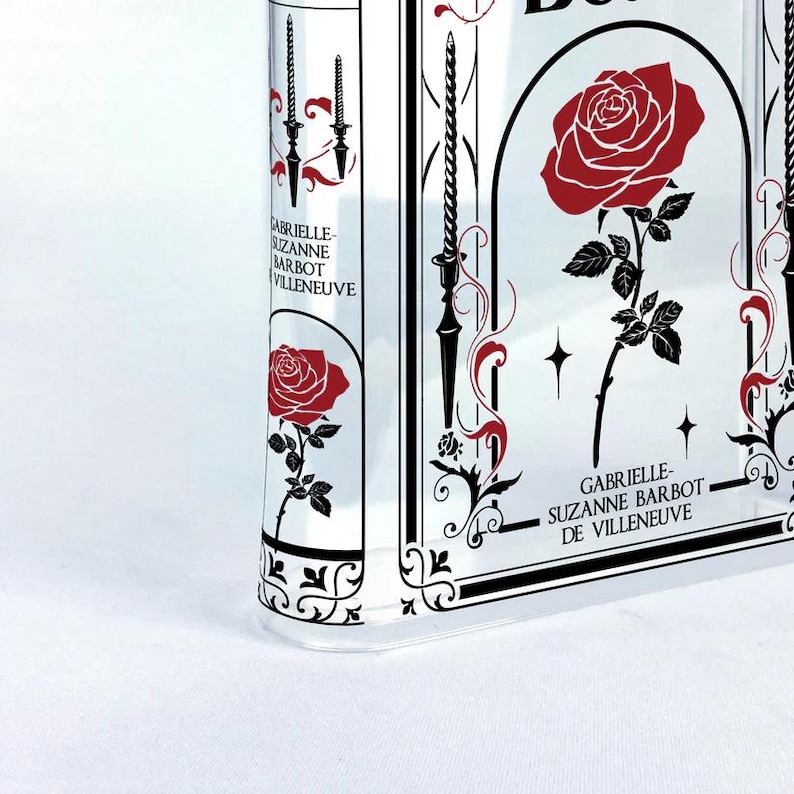 K&ouml;nnte beinhalten: Ein klares Glasbuch mit einem schwarz-wei&szlig;en Blumendesign und einer roten Rose. Der Text auf dem Buch lautet "Gabrielle-Suzanne Barbot de Villeneuve".