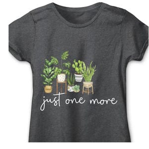 Puede incluir: Camiseta gris oscuro con una ilustraci&oacute;n de acuarela de varias plantas en macetas, incluyendo una monstera, un cactus y una sansevieria. La frase "just one more" est&aacute; escrita en cursiva debajo de las plantas.