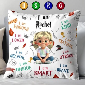 May include: White decorative pillow featuring a cartoon girl with glasses, the name "Rachel", and inspirational phrases like "I am Smart" and "I am Brave". The pillow has a variety of small illustrations.