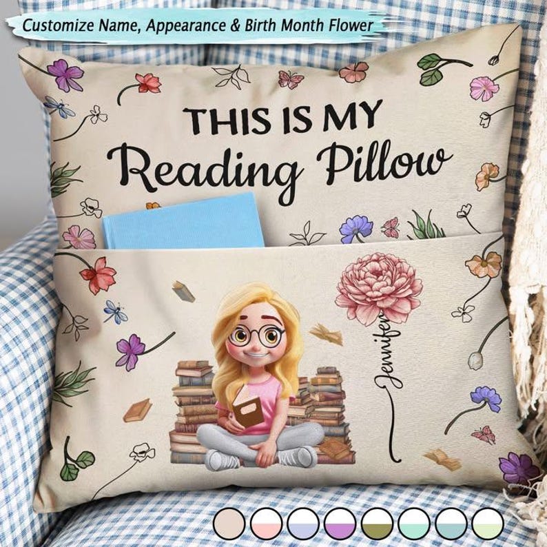 May include: A beige reading pillow with the text "THIS IS MY Reading Pillow". It features a cartoon illustration of a girl with glasses sitting on books, a pocket, and floral accents. The pillow is customisable.
