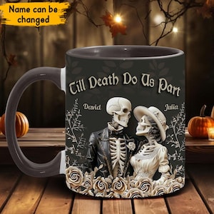 Pode incluir: Caneca de café preta com alça branca. A caneca tem uma ilustração em preto e branco de dois esqueletos vestidos de noiva e noivo. O texto "Till Death Do Us Part" está impresso na caneca, juntamente com os nomes "David" e "Julia".