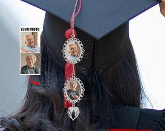 May include: A graduation cap tassel with two silver photo frames and a silver angel wing charm. The photo frames are attached to a red cord. The text "YOUR PHOTO" is visible in the image.