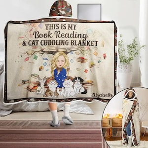 Może przedstawiać: Kapturowy koc z fantazyjnym wzorem przedstawiającym kobietę, koty i książki. Koc ma napis "THIS IS MY Book Reading & Cat Cuddling BLANKET". Kaptur i obramowanie mają brązowy wzór. Koc jest beżowy z białym, puszystym wnętrzem.