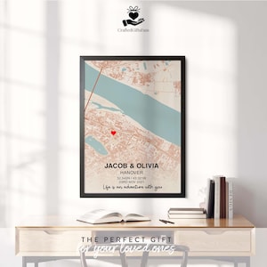 May include: A framed map print featuring a city map with a red heart marker. The text "JACOB & OLIVIA" and "HANOVER" are displayed, along with coordinates and a date. The phrase "Life is an adventure with you" is also included.