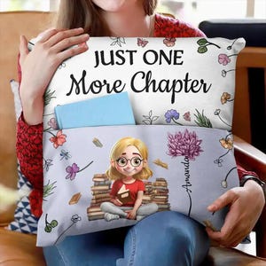 May include: A white pillow with the text "JUST ONE More Chapter" and floral designs. The bottom section features a cartoon girl with glasses holding a book, a stack of books, and the name "Amanda". A light blue book is in the pocket.