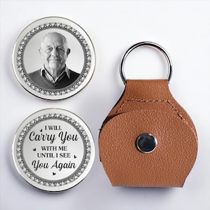 Puede incluir: Un recuerdo conmemorativo plateado con una foto de un hombre y un llavero con un llavero de cuero marrón. El recuerdo tiene un borde decorativo y el texto "I WILL Carry You with Me Until I See You Again."
