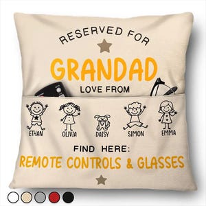 Puede incluir: Cojín beige con el texto "RESERVED FOR GRANDAD" en negro y amarillo. Debajo están las palabras "LOVE FROM" y los nombres Ethan, Olivia, Daisy, Simon y Emma. También se ve el texto "FIND HERE: REMOTE CONTROLS & GLASSES".
