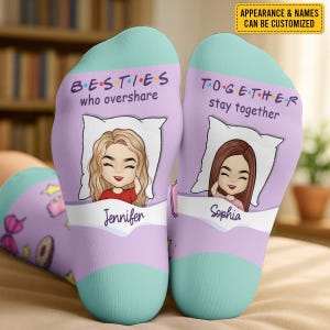 May include: A pair of custom socks with a light purple background and teal toes. One sock reads "BESTIES who overshare" and features a cartoon of a blonde woman named Jennifer. The other sock reads "TOGETHER stay together" with a cartoon of a brunette woman named Sophia.