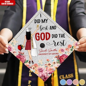 以下が含まれることがあります： 銀色のグリッターの背景と花のアクセントが付いた卒業帽。帽子には「私は最善を尽くし、神は残りを成し遂げた」というテキストが印刷されています。帽子には「2025年卒業」と「サラ・スミス、オックスフォード大学」のテキストも含まれています。