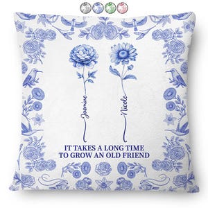 May include: White throw pillow with a blue floral design. Features two stylized flowers with the names "Jasmine" and "Nicole" below them. The text "IT TAKES A LONG TIME TO GROW AN OLD FRIEND" is also included.