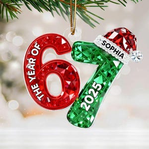 May include: A Christmas ornament with the numbers 6 and 7 in red and green, respectively. The number 6 has the text "THE YEAR OF" and the number 7 has the year "2025". A Santa hat with the name "SOPHIA" is on top of the number 7.