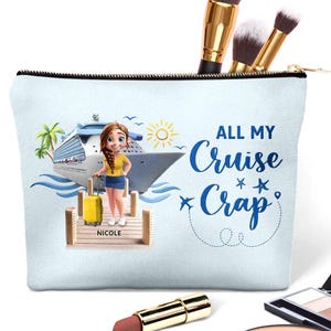 Könnte beinhalten: Hellblaue Kosmetiktasche mit schwarzem Reißverschluss, mit einer Cartoon-Illustration einer Frau mit gelbem Koffer auf einem Steg vor einem Kreuzfahrtschiff. Text: "ALL MY Cruise Crap".