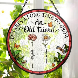 May include: A round stained glass window hanging with a red border. It features a white background with the text "It takes a long time to grow an old friend". There are three flowers with butterflies and dragonflies around them. The flowers are labeled "Elizabeth", "Caroline", and "
