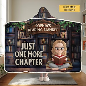 May include: A hooded reading blanket featuring a library scene with the text "Sophia's Reading Blanket" and "Just One More Chapter." The design includes a cartoon illustration of a person reading a book. The blanket is customizable.
