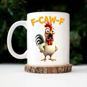 May include: White ceramic mug featuring a cartoon rooster with an open beak and the text "F-CAW-F" in yellow. The rooster has red comb and wattle, with a black and white tail. The mug sits on a wooden coaster.