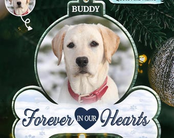 May include: White bone-shaped Christmas bauble with a blue paw print design. The bauble has a photo of a dog with a red collar and the words "Forever in Our Hearts" in blue text. The bauble also has the word "Buddy" in blue text.