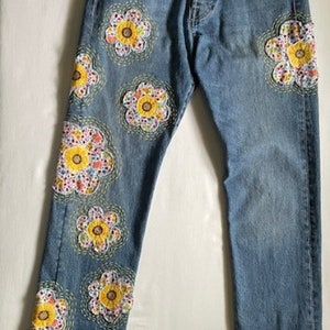 May include: Blue denim jeans with colourful embroidered flowers on the left leg.