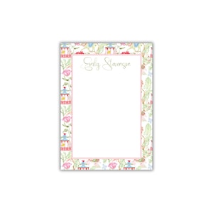 May include: White notepad with a pink border featuring a repeating pattern of colorful pagodas and flowers. The notepad has a line for a name and the name "Emily Stevenson" is written in cursive.