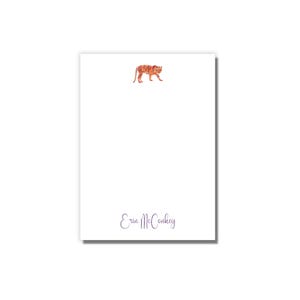 May include: White notepad with a watercolor illustration of an orange tiger in the top center. The bottom of the notepad has the name "Erin McConkey" written in purple.