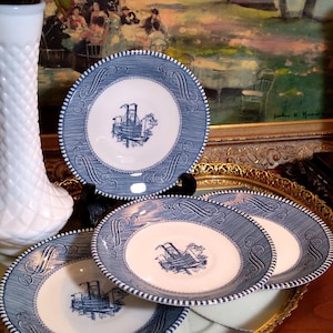 May include: Set of four blue and white ceramic saucers with a blue and white ship design. The saucers are stacked on a gold tray.