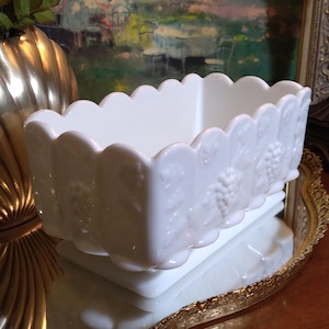 May include: White milk glass planter with a scalloped rim and grapevine design. The planter is sitting on a gold-colored tray.