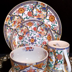 May include: A set of Japanese-style porcelain tableware featuring a floral design in red, yellow, and blue. The set includes plates, a bowl, and a mug, all with intricate patterns and gold trim.