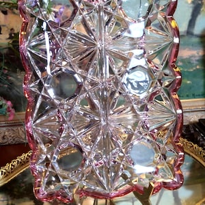 May include: A vintage glass trinket tray with a pink rim and a starburst pattern. The tray is on a gold metal stand.
