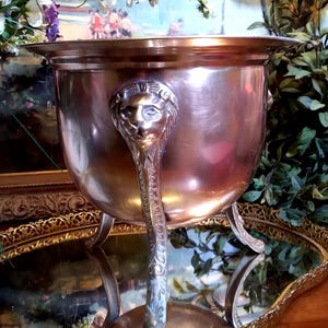 May include: A gold-toned metal serving bowl with three lion head handles. The bowl is sitting on a gold-toned metal tray with a decorative edge.
